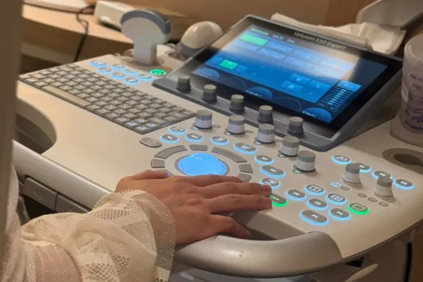 Mãos da médica operando o painel de controle do equipamento de ultrassom.